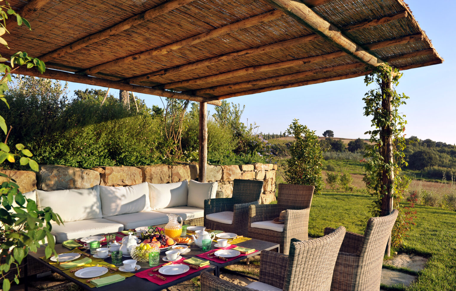 Outdoor dining area featuring a rustic wooden pergola, comfortable seating, and a beautifully set table with a variety of dishes and fresh fruits, surrounded by lush greenery and scenic views. Ideal for alfresco meals and gatherings. | Only on SopranoVillas
