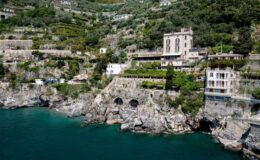 Coastal view of luxury villas and terraced gardens along the cliffs of the Amalfi Coast, Italy, with clear turquoise waters below.