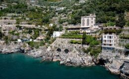 Coastal view of cliffside houses along the Amalfi Coast, showcasing lush greenery and rocky formations near the turquoise sea.