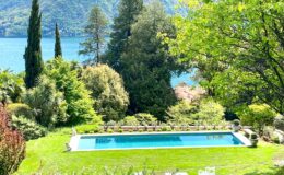 Scenic view of a lush garden with a swimming pool overlooking a serene lake, surrounded by mountains and greenery, ideal for relaxation and outdoor activities.