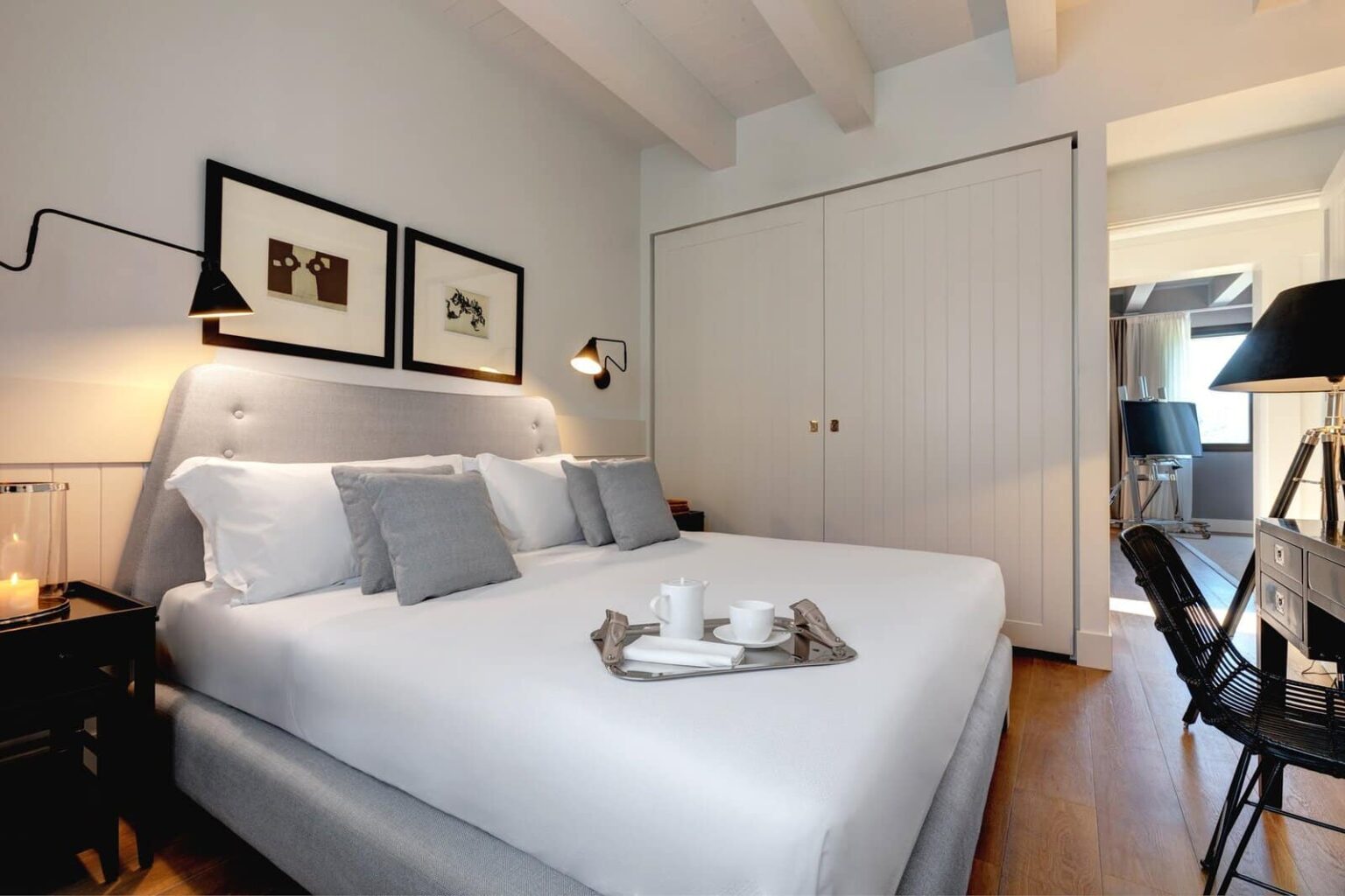 Cozy and modern bedroom featuring a comfortable double bed with gray pillows, elegant wall art, and a neatly arranged breakfast tray. The room has ample natural light, wooden flooring, and a spacious closet, creating a welcoming atmosphere for relaxation. | Only on SopranoVillas