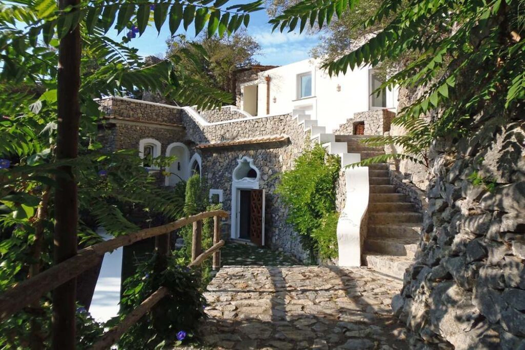 Charming stone pathway leading to a modern villa surrounded by lush greenery, featuring a staircase and terraced landscaping in a serene outdoor setting. | Only on SopranoVillas