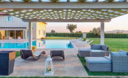 Luxury outdoor living space featuring a modern pergola, comfortable seating, and a pristine swimming pool surrounded by lush greenery. Ideal for relaxation and entertaining in a serene setting.