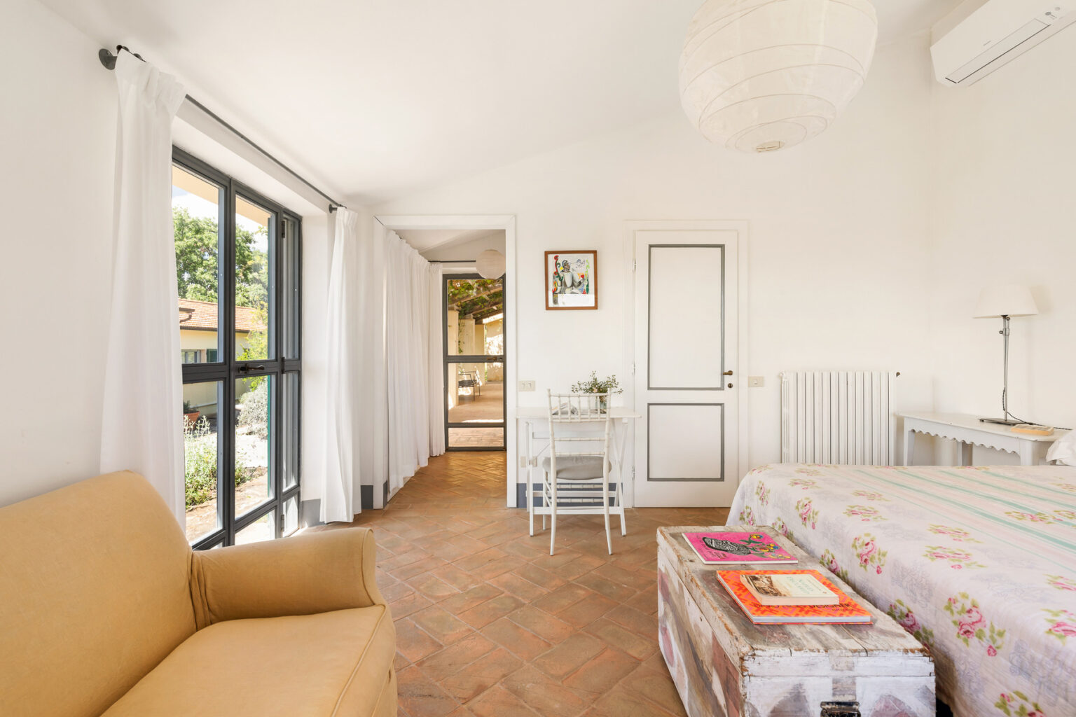 Cozy and bright bedroom featuring a comfortable sofa, a small dining table, and large windows with natural light. The decor includes floral patterns and a relaxed atmosphere, ideal for a peaceful getaway. | Only on SopranoVillas