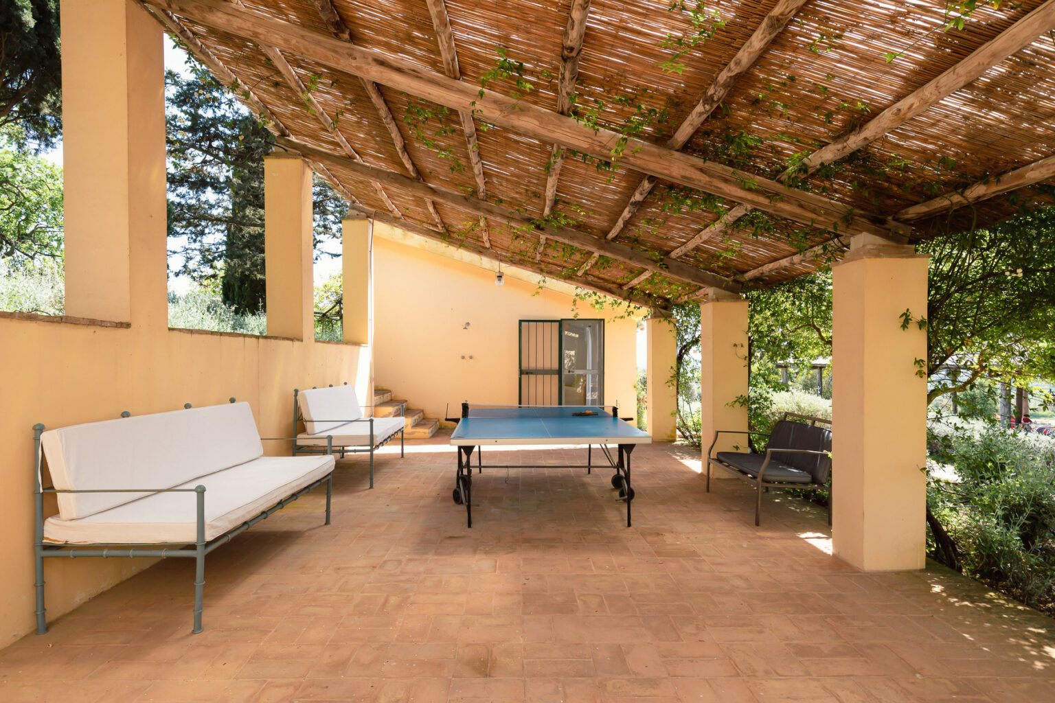 Outdoor patio area featuring a ping pong table, comfortable seating, and a shaded roof with greenery, ideal for relaxation and entertainment. | Only on SopranoVillas