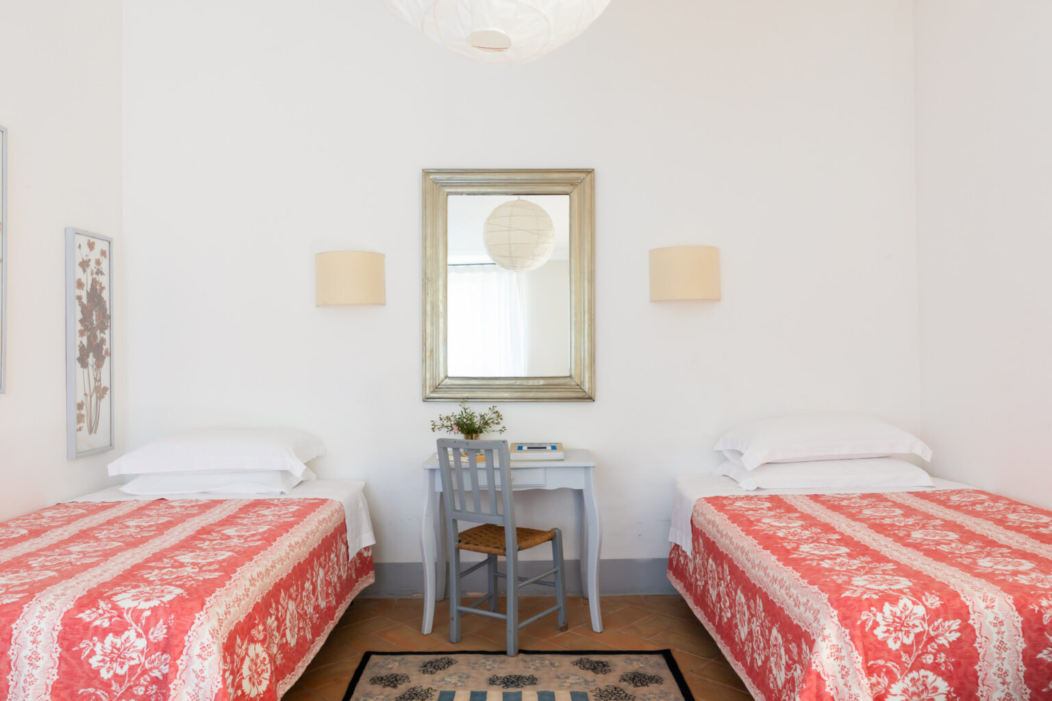 Cozy bedroom featuring two twin beds with red floral bedding, a small desk with a chair, and a decorative mirror on the wall, designed for comfort and relaxation. | Only on SopranoVillas