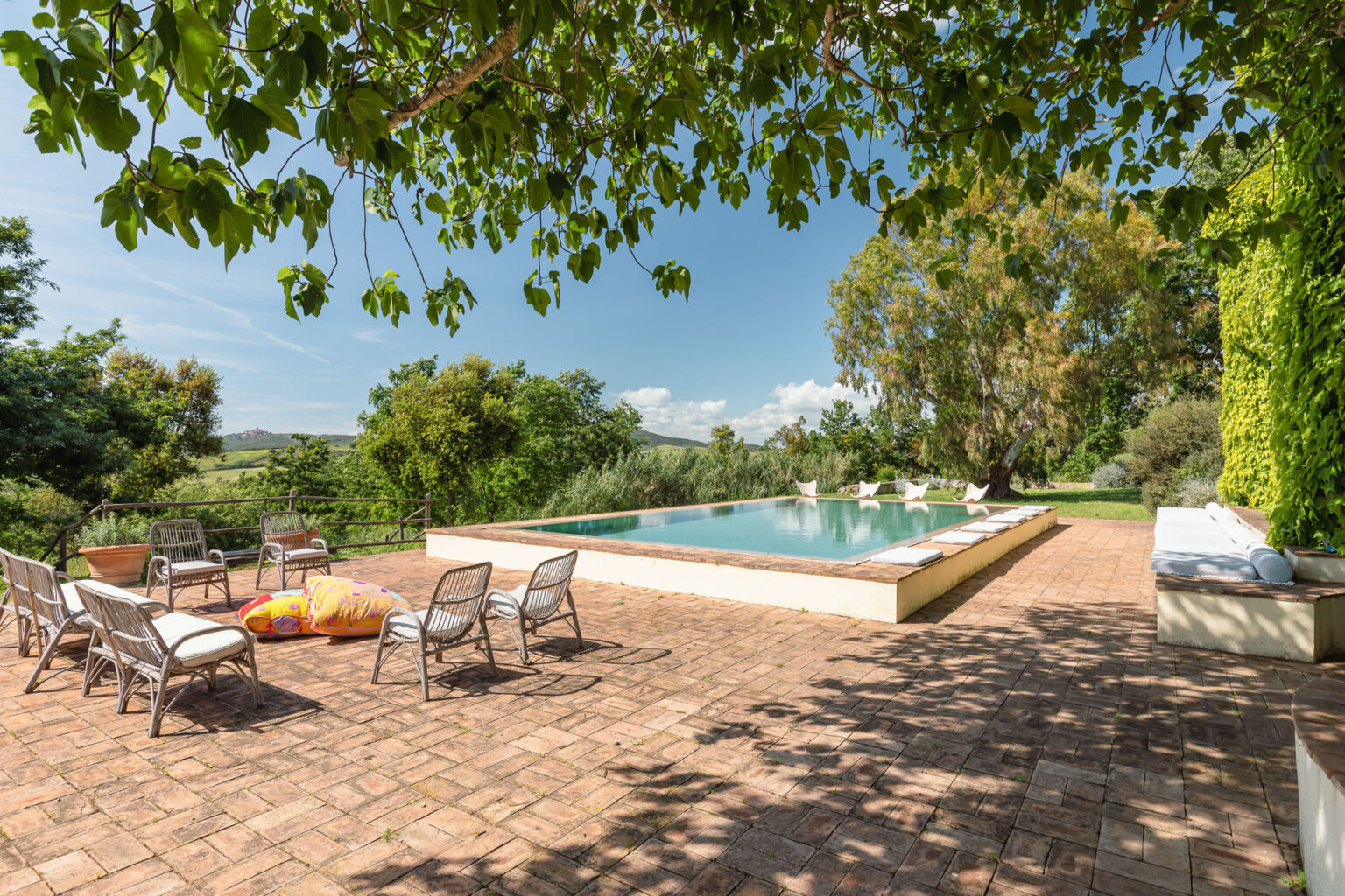 Serene outdoor pool area surrounded by lush greenery, featuring lounge chairs and a spacious patio, perfect for relaxation and leisure in a sunny environment. | Only on SopranoVillas