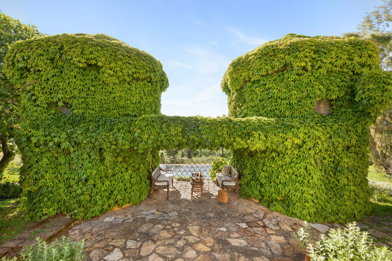 Lush green ivy-covered structures create a unique outdoor dining area with stone pathways and rustic furniture, surrounded by nature. | Only on SopranoVillas