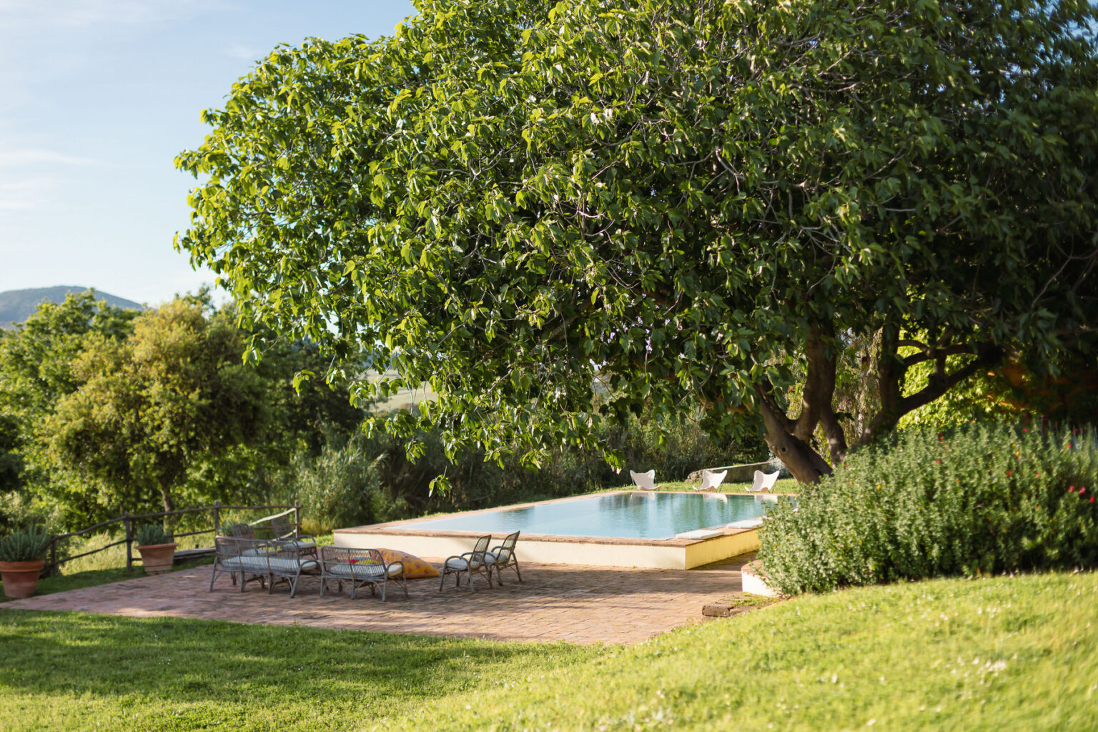Scenic outdoor pool area surrounded by lush greenery, featuring a large tree, comfortable seating, and a serene landscape. Ideal for relaxation and leisure activities. | Only on SopranoVillas