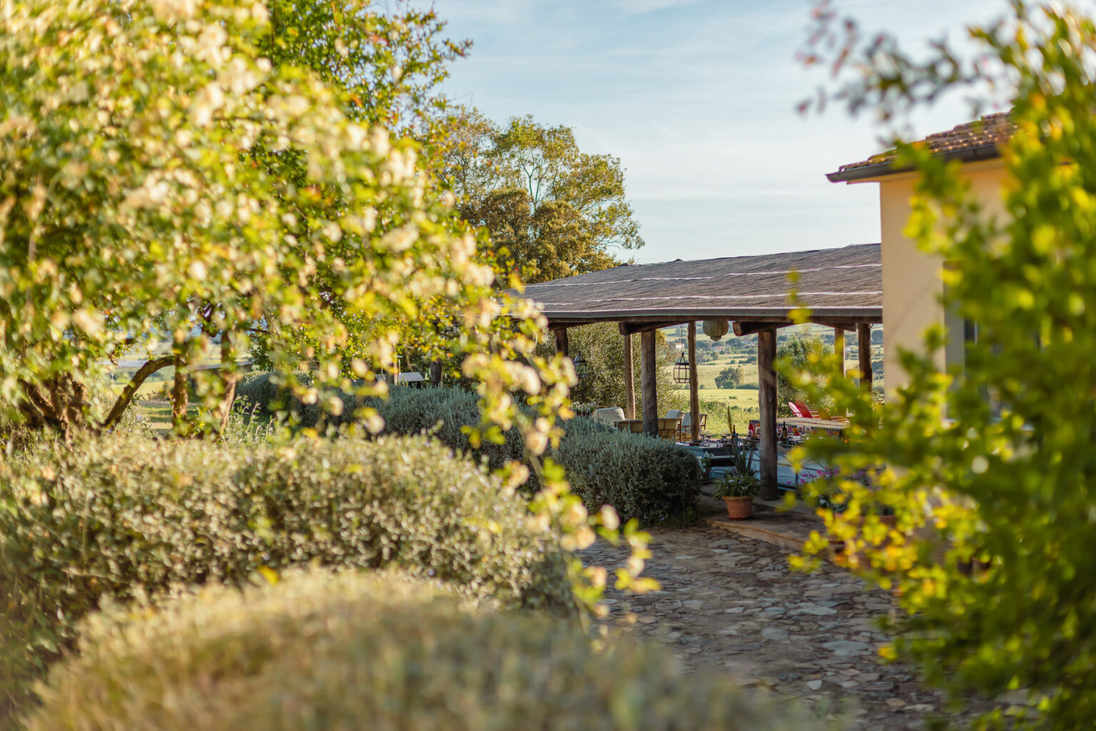 Charming countryside view featuring a rustic house with a covered porch, surrounded by lush greenery and flowering plants in a serene outdoor setting. | Only on SopranoVillas