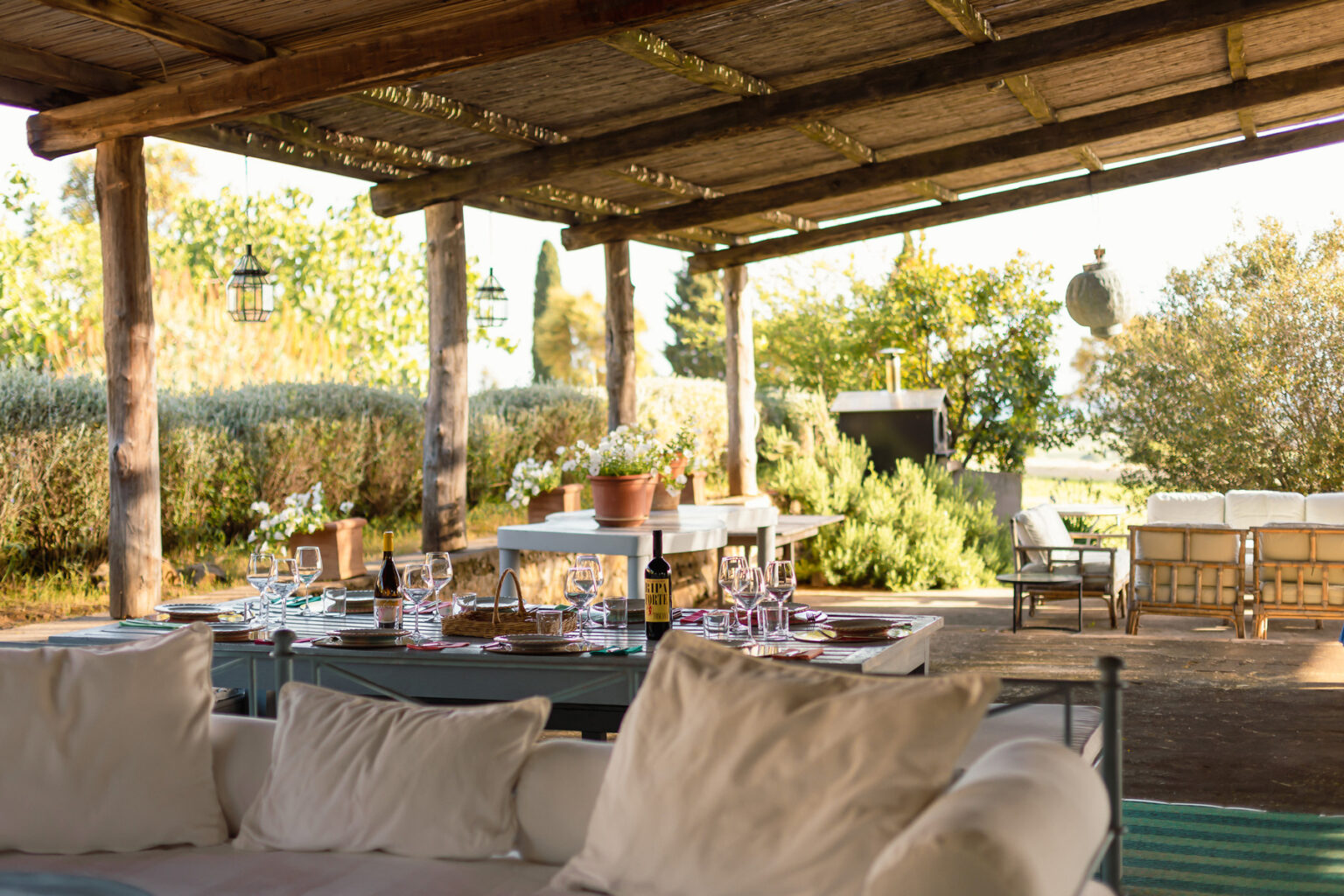 Cozy outdoor dining area featuring a rustic wooden pergola, comfortable seating, and a beautifully set table surrounded by greenery, perfect for gatherings and alfresco meals. | Only on SopranoVillas