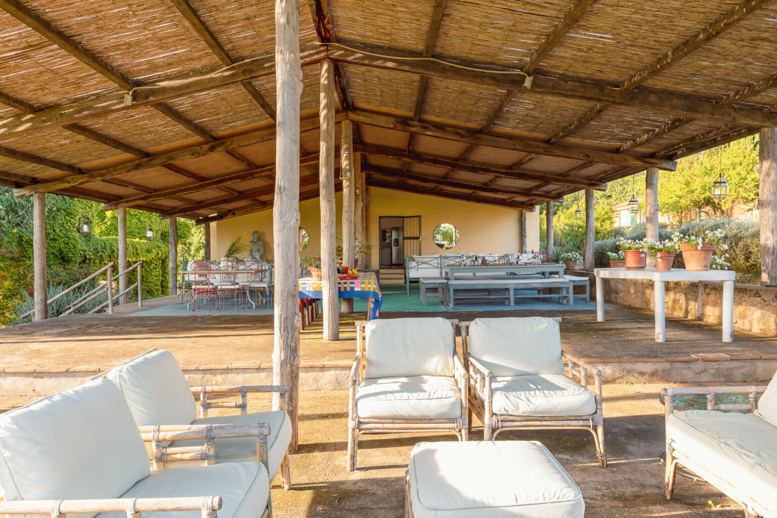 Outdoor lounge area with comfortable seating under a thatched roof, featuring wooden pillars and a spacious layout, ideal for relaxation and social gatherings. | Only on SopranoVillas