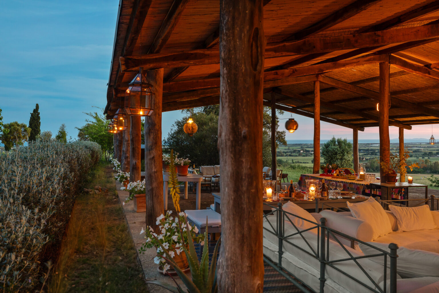 Cozy outdoor seating area with rustic wooden beams, soft lighting, and scenic views of the countryside, perfect for relaxation and gatherings at dusk. | Only on SopranoVillas