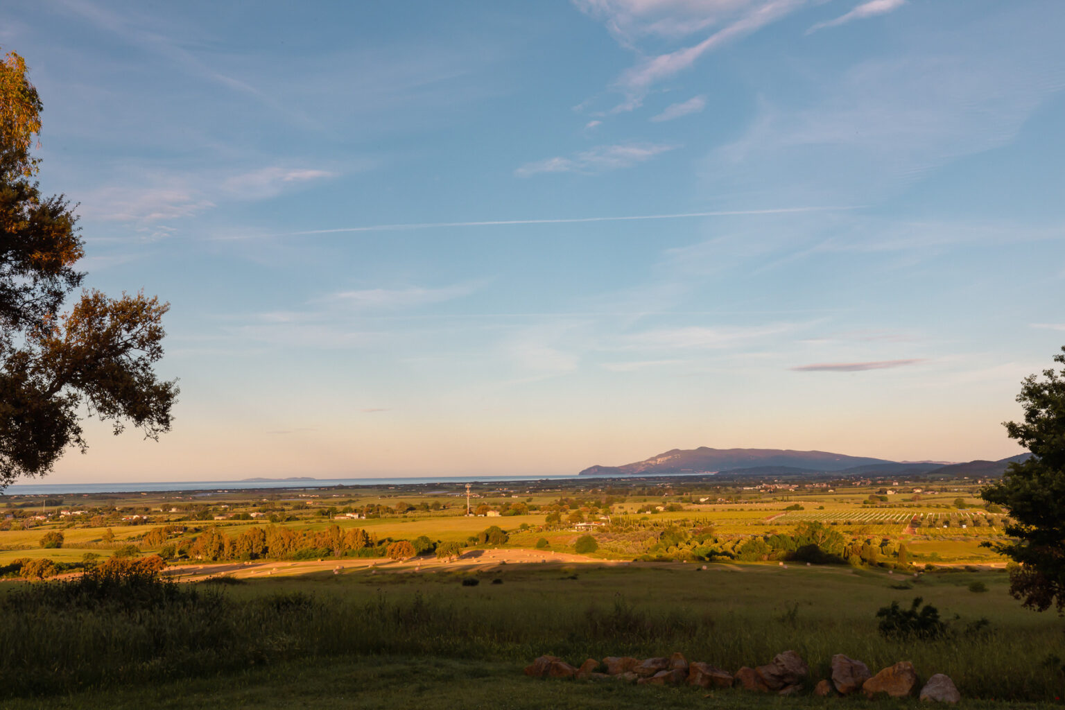 Scenic landscape view featuring rolling hills, lush greenery, and a distant mountain range under a clear blue sky with wispy clouds. The image captures the tranquility of nature and the beauty of the outdoors during sunset. | Only on SopranoVillas