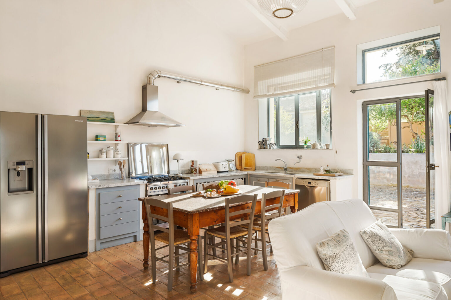 Bright and airy kitchen featuring a wooden dining table, stainless steel appliances, and large windows that allow natural light to fill the space. The design combines modern and rustic elements, creating a welcoming atmosphere. | Only on SopranoVillas