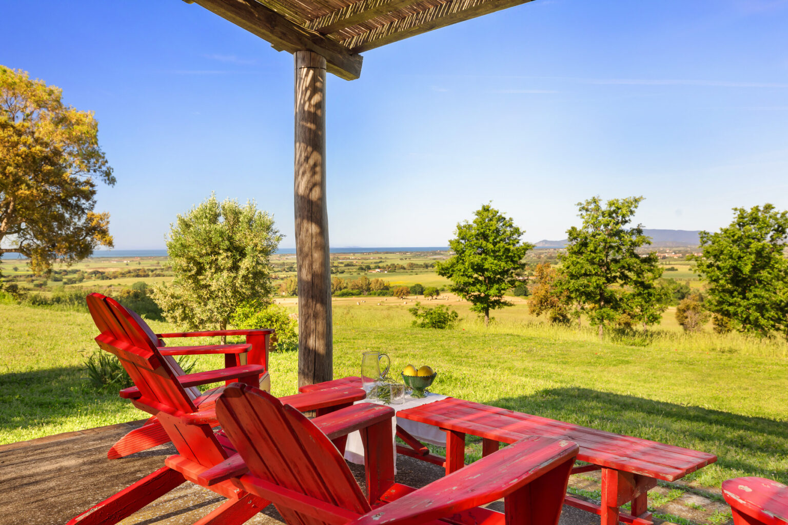 Scenic outdoor view featuring red Adirondack chairs on a wooden deck, overlooking a lush green landscape and blue sky. Ideal for relaxation and enjoying nature. | Only on SopranoVillas