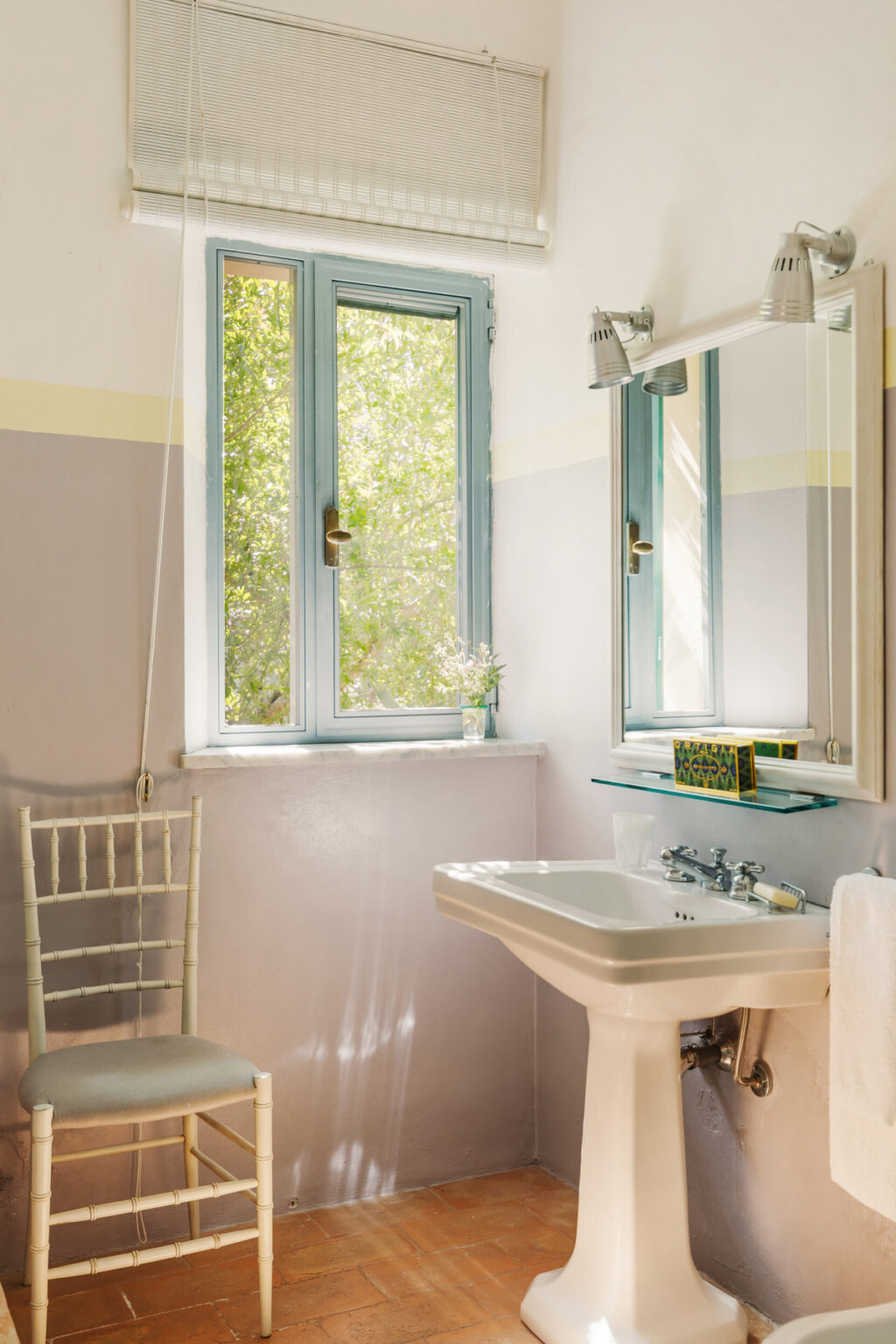 Bright and airy bathroom featuring large windows with blue frames, a modern sink, and a minimalist design. Natural light floods the space, complemented by soft pastel wall colors and a touch of greenery. | Only on SopranoVillas