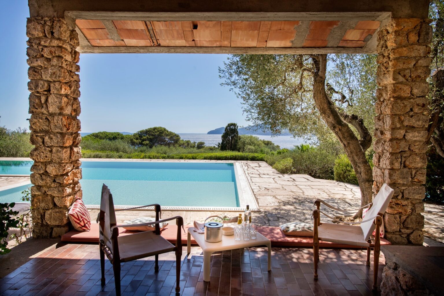 Scenic view from a stone patio overlooking a swimming pool, surrounded by lush greenery and a serene landscape, perfect for relaxation and outdoor living. | Only on SopranoVillas