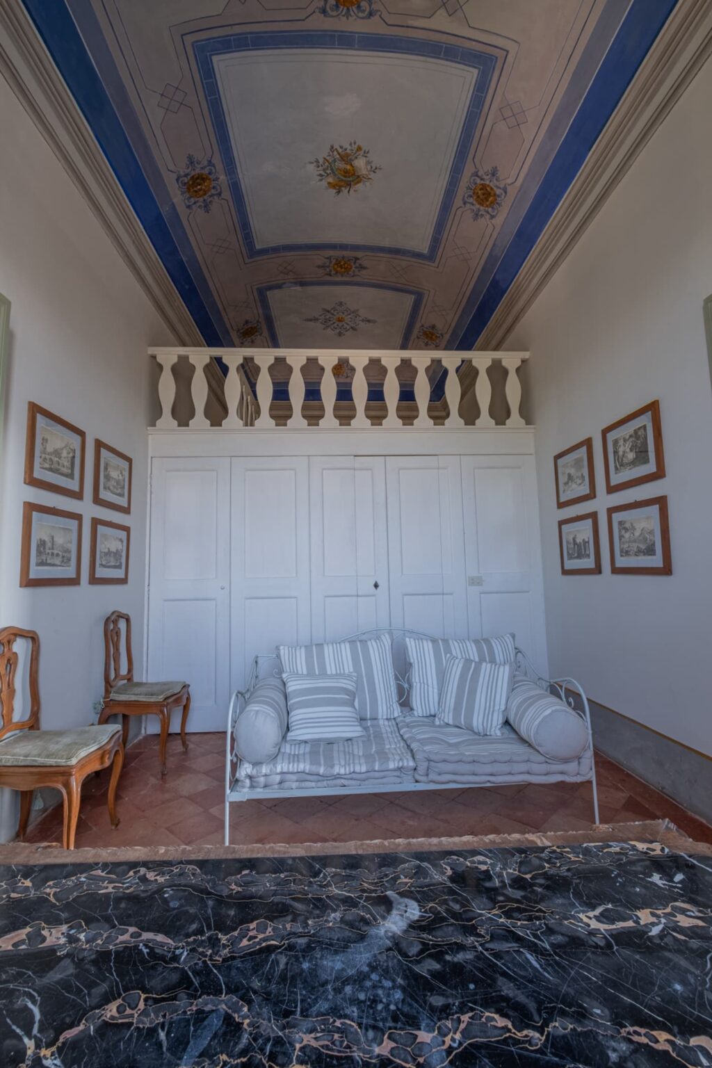 Cozy living room interior featuring a white sofa with striped cushions, framed artworks on the walls, and a decorative balcony above, showcasing a blend of modern comfort and artistic charm. | Only on SopranoVillas