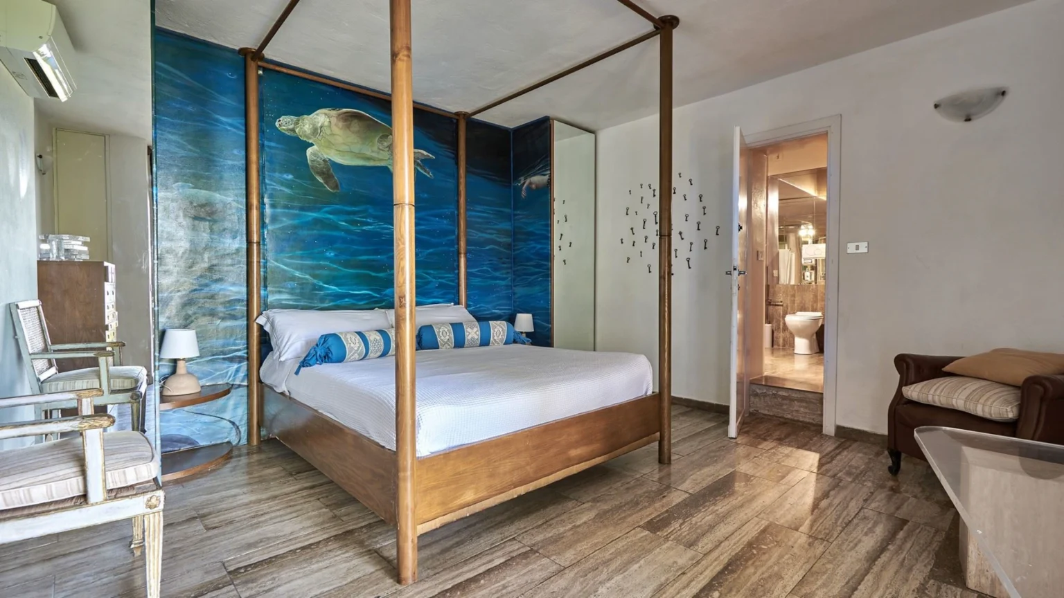 Cozy bedroom featuring a four-poster bed with blue and white accents, a mural of a turtle on a blue ocean background, stylish wooden furniture, and a modern bathroom entrance, ideal for a relaxing getaway. | Only on SopranoVillas