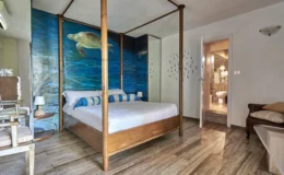 Cozy bedroom featuring a four-poster bed with blue and white accents, a mural of a turtle on a blue ocean background, stylish wooden furniture, and a modern bathroom entrance, ideal for a relaxing getaway.