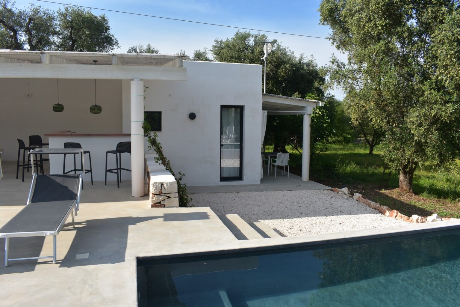 Modern villa with a swimming pool, outdoor seating area, and lush greenery in the background, showcasing a blend of contemporary architecture and natural surroundings. | Only on SopranoVillas