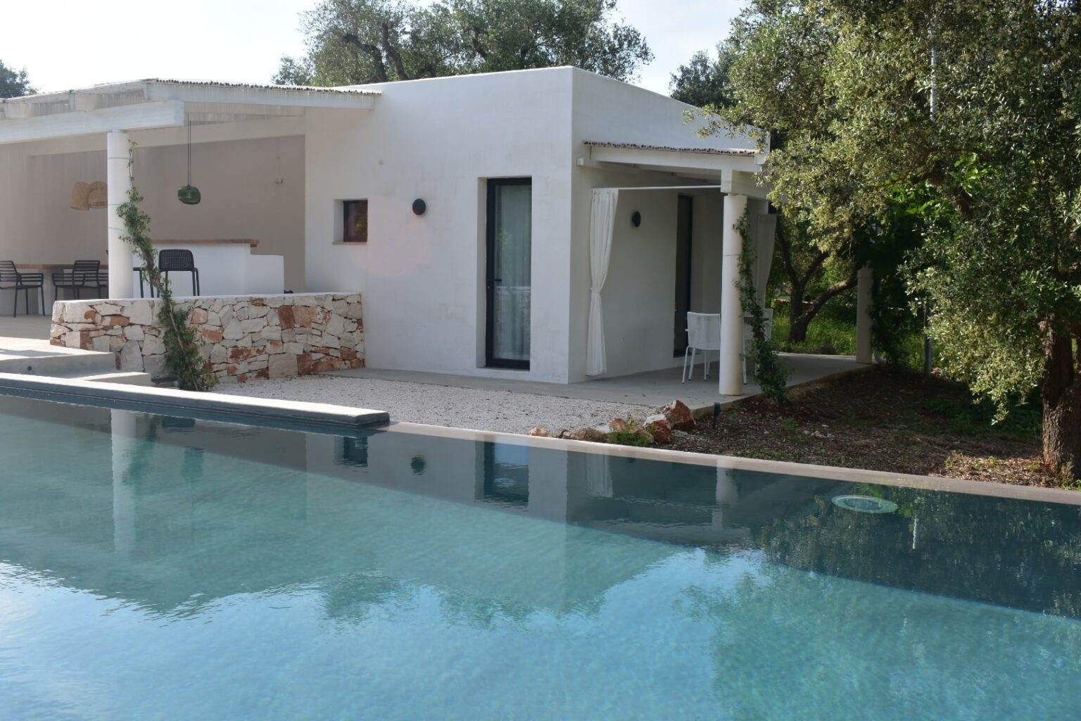 Modern white villa with a swimming pool, surrounded by greenery and olive trees, featuring a spacious outdoor area and contemporary architecture. | Only on SopranoVillas