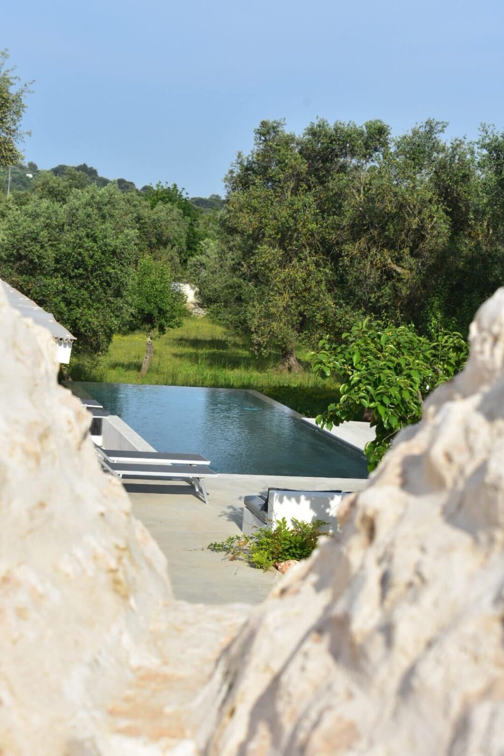 Modern infinity pool surrounded by lush greenery, featuring comfortable loungers and a serene landscape view. Ideal for luxury retreats and outdoor relaxation. | Only on SopranoVillas