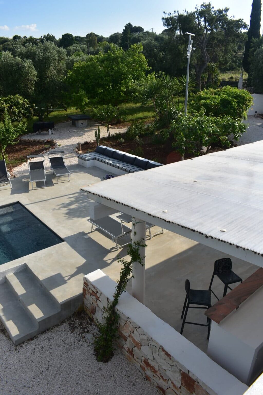 Modern outdoor space featuring a swimming pool, lounge chairs, and a stylish patio area surrounded by lush greenery, ideal for relaxation and entertainment. | Only on SopranoVillas
