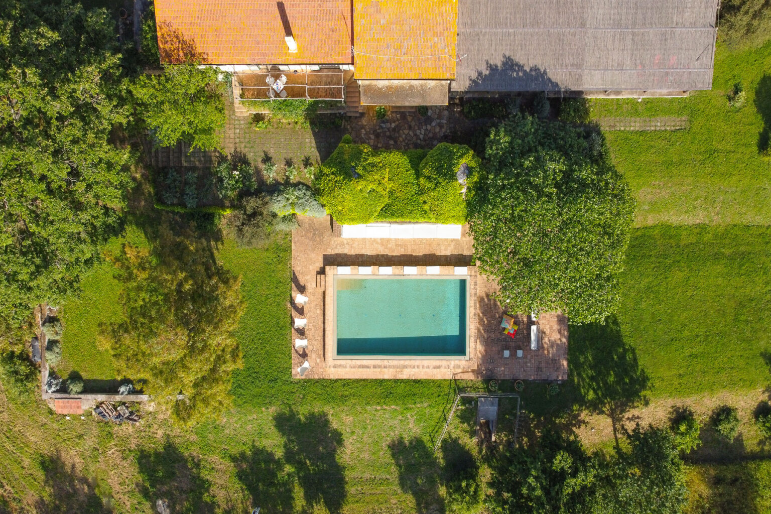 Aerial view of a residential property featuring a rectangular swimming pool surrounded by lush greenery and patio furniture, highlighting a tranquil outdoor setting. | Only on SopranoVillas