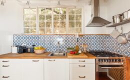 Modern kitchen with blue patterned backsplash, wooden countertops, and stainless steel appliances, featuring fresh fruits and a well-organized layout.