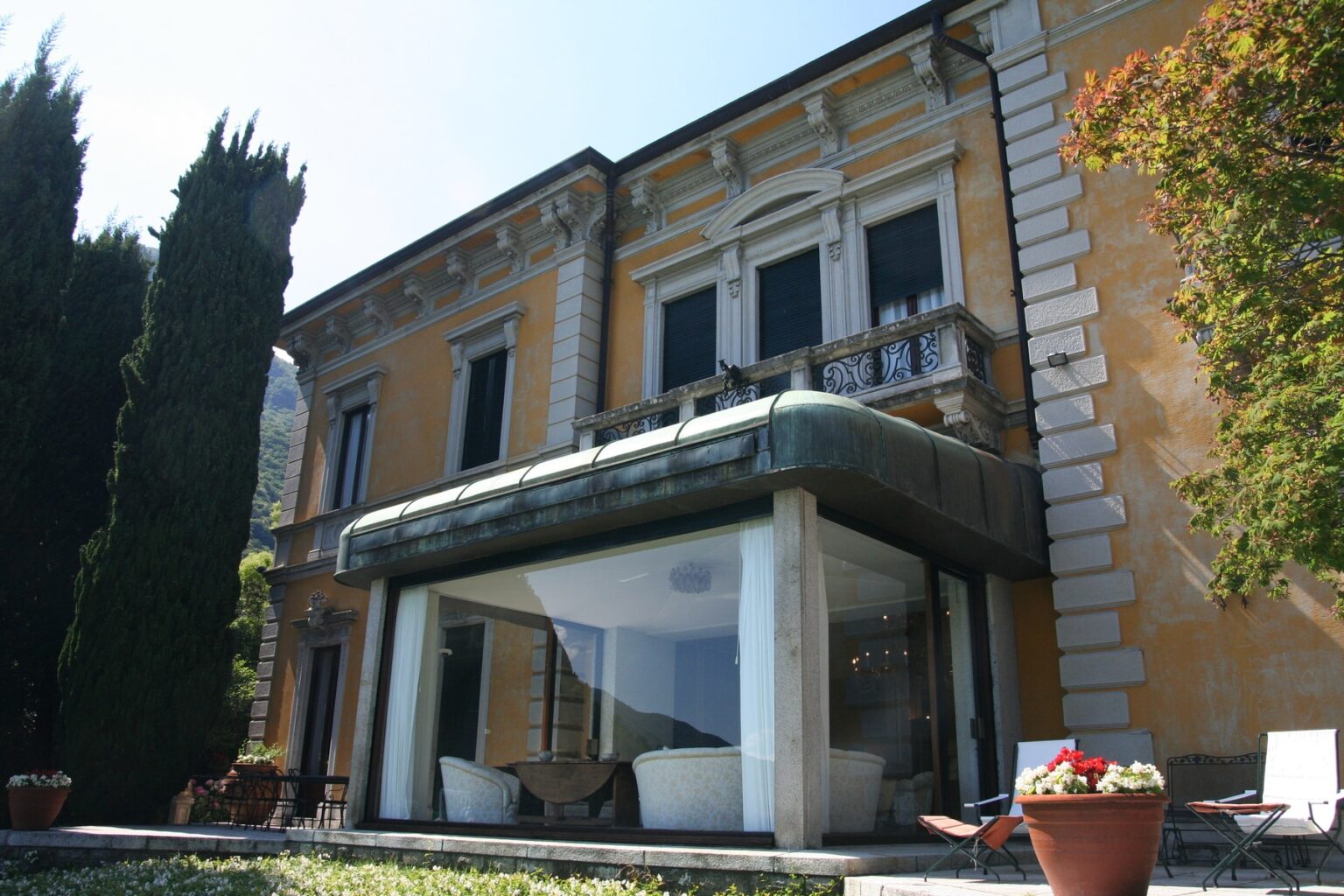 Elegant villa with a modern glass extension, showcasing classic architecture and lush greenery in the surrounding garden. | Only on SopranoVillas