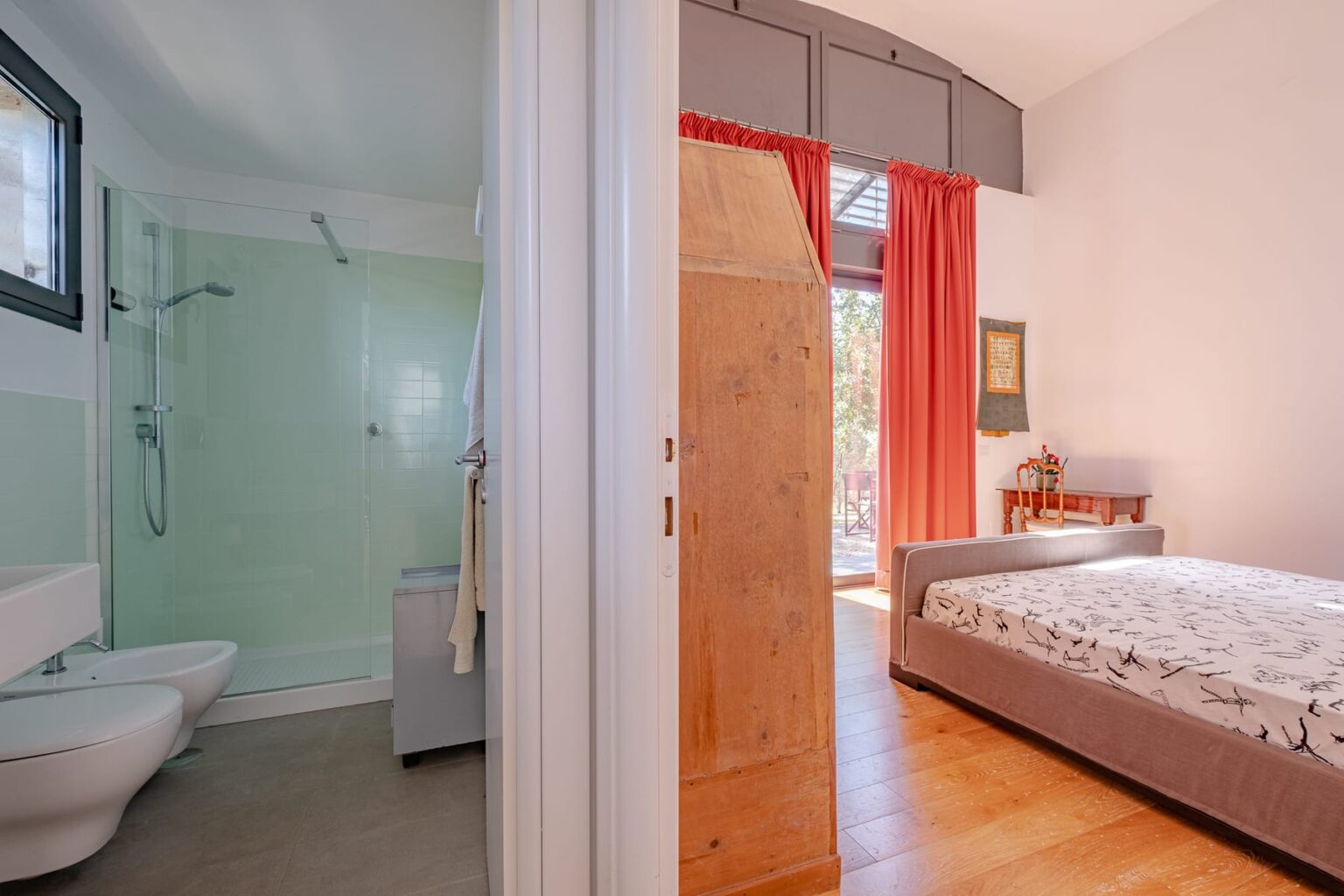 Modern bathroom and bedroom interior showcasing a stylish design with natural light, featuring a shower, toilet, and a comfortable bed with decorative bedding. | Only on SopranoVillas