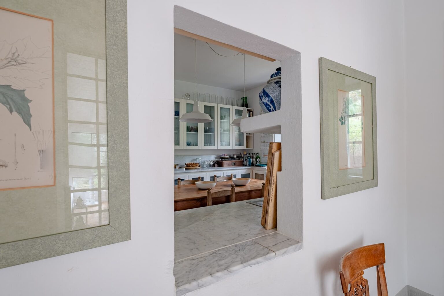 Interior view of a dining area with wooden furniture, framed artwork on the walls, and an open kitchen in the background, showcasing a modern, inviting design. | Only on SopranoVillas