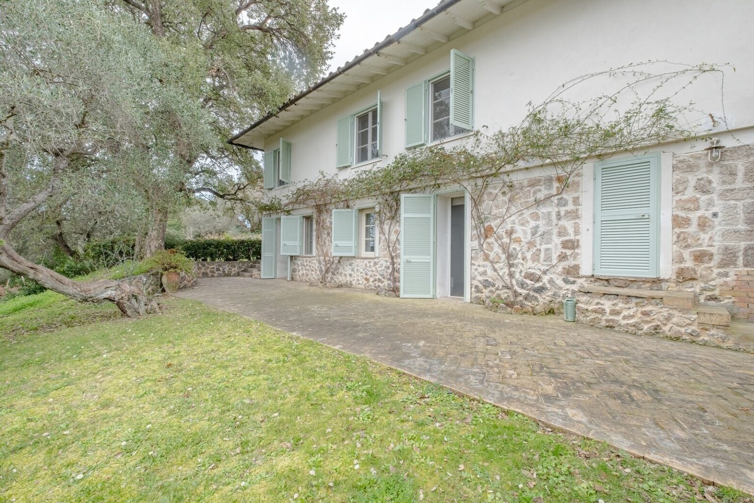 Charming stone house with green shutters surrounded by lush greenery and a paved patio, featuring a tranquil outdoor space perfect for relaxation. | Only on SopranoVillas