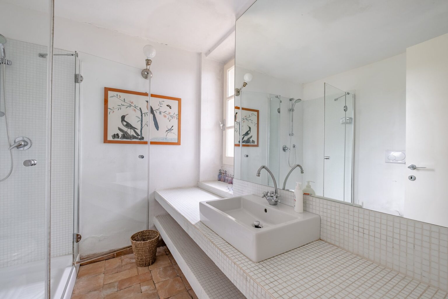 Modern bathroom featuring a spacious design, glass shower enclosure, minimalist sink, and natural light. Decorated with artwork and neutral tones, it combines functionality with aesthetic appeal. | Only on SopranoVillas