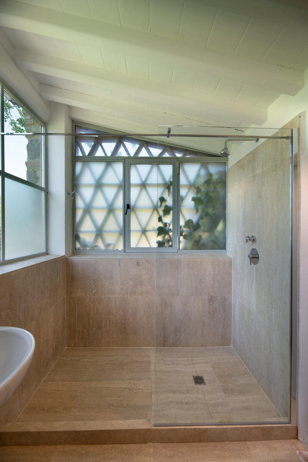 Modern bathroom featuring a spacious walk-in shower with glass enclosure, natural stone tiles, and large windows allowing natural light. The design highlights a minimalist aesthetic with a sleek showerhead and a clean, uncluttered space. | Only on SopranoVillas