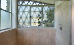 Modern bathroom featuring a spacious walk-in shower with glass enclosure, natural stone tiles, and large windows allowing natural light. The design highlights a minimalist aesthetic with a sleek showerhead and a clean, uncluttered space.