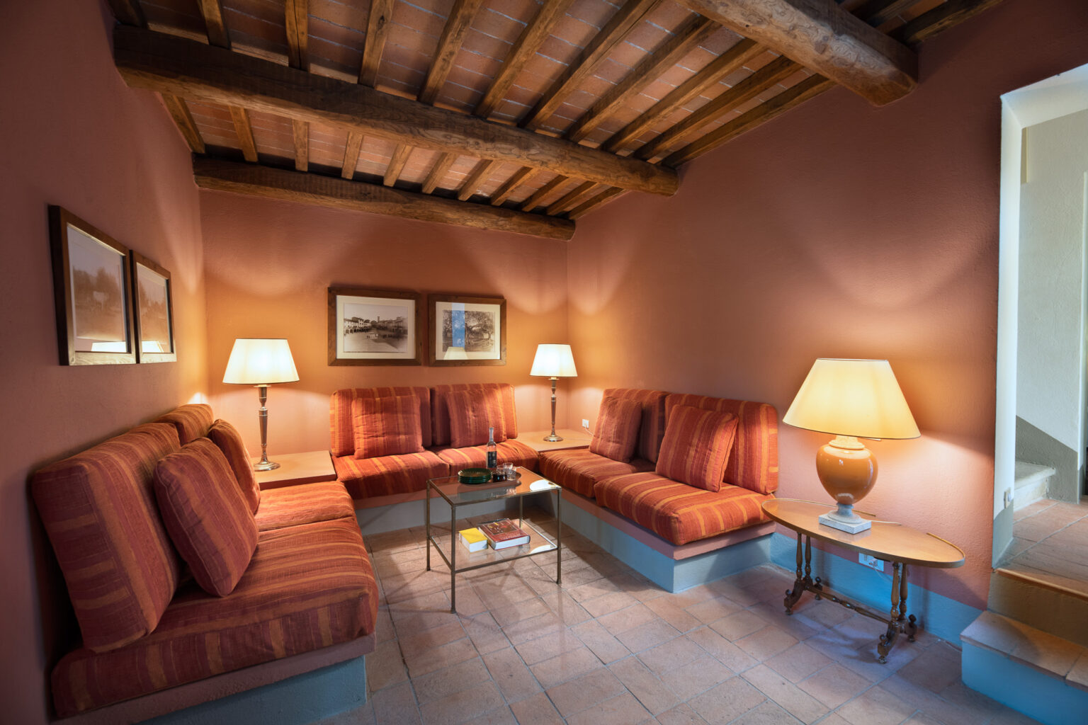 Cozy living room with striped seating, warm lighting, and rustic wooden beams, featuring framed artwork and a glass coffee table. Ideal for relaxation and social gatherings. | Only on SopranoVillas