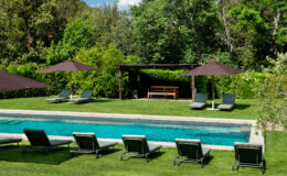 Luxurious outdoor pool area featuring comfortable lounge chairs, shaded by large umbrellas, surrounded by lush greenery and a cozy seating area under a pergola. Ideal for relaxation and leisure.