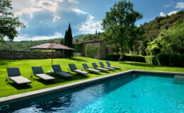 Luxury outdoor pool area featuring comfortable lounge chairs and a shaded umbrella, surrounded by lush greenery and scenic hills, perfect for relaxation and leisure.