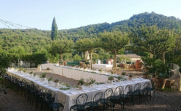 Outdoor dining setup with a long table elegantly arranged for an event, surrounded by lush greenery and hills, creating a picturesque setting.