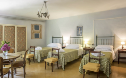 Cozy hotel room featuring two twin beds with patterned bedspreads, a wooden table and chairs, and soft lighting. Ideal for families or groups seeking comfortable accommodations.