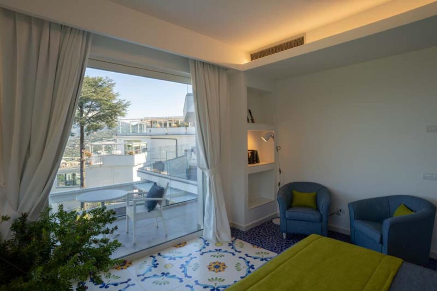 Cozy modern living room featuring large windows with scenic views, bright blue armchairs, and decorative plants, complemented by colorful tiled flooring. | Only on SopranoVillas
