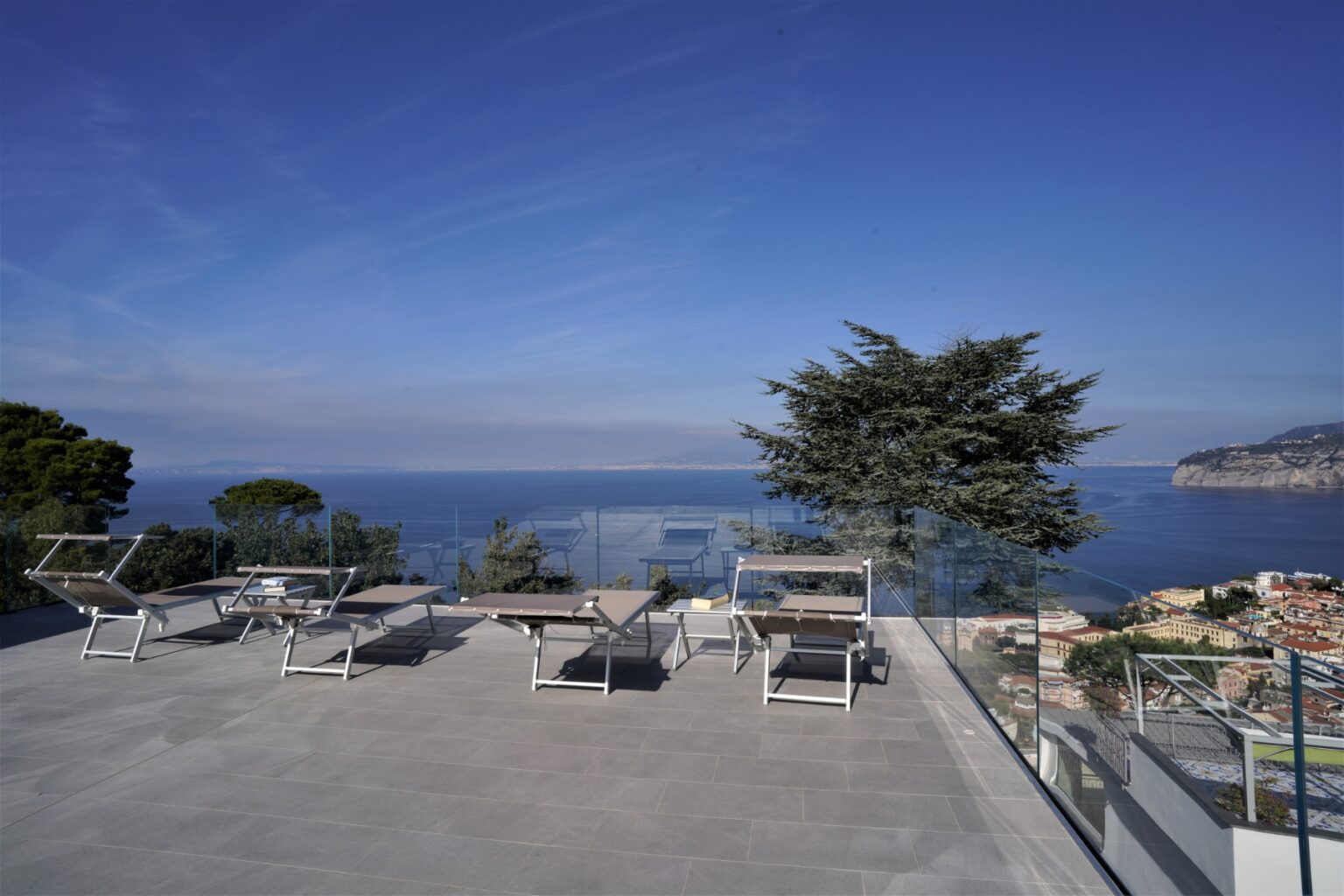 Modern terrace with lounge chairs overlooking a serene ocean view and clear blue sky, ideal for relaxation and outdoor gatherings. | Only on SopranoVillas
