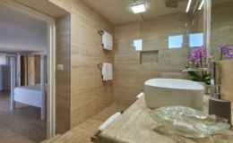 Modern bathroom design featuring natural stone walls, a glass shower enclosure, and a stylish countertop with a white sink. The decor includes fresh orchids and neatly arranged towels, creating a serene and elegant atmosphere.