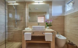 Modern bathroom featuring natural stone walls, a sleek glass shower, a stylish vessel sink on a wooden vanity, fresh orchids as decor, and elegant white towels.
