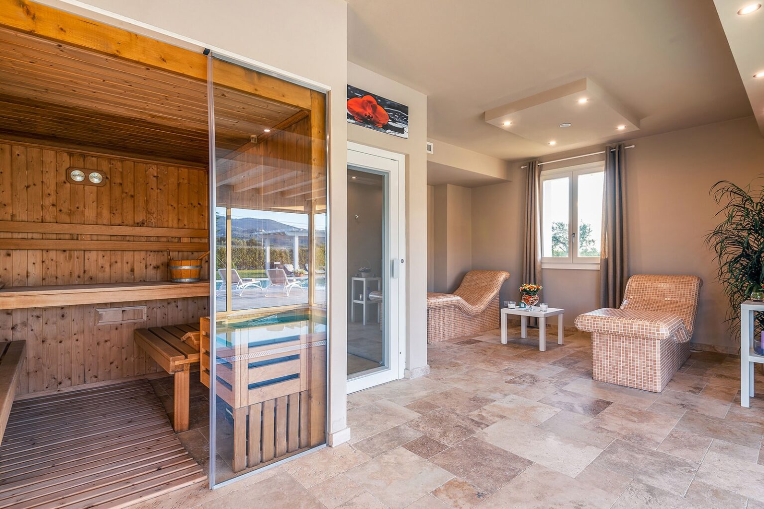 Interior view of a modern sauna room featuring wooden benches, glass doors, and relaxing lounge chairs, designed for wellness and relaxation. | Only on SopranoVillas