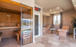 Interior view of a modern sauna room featuring wooden benches, glass doors, and relaxing lounge chairs, designed for wellness and relaxation.