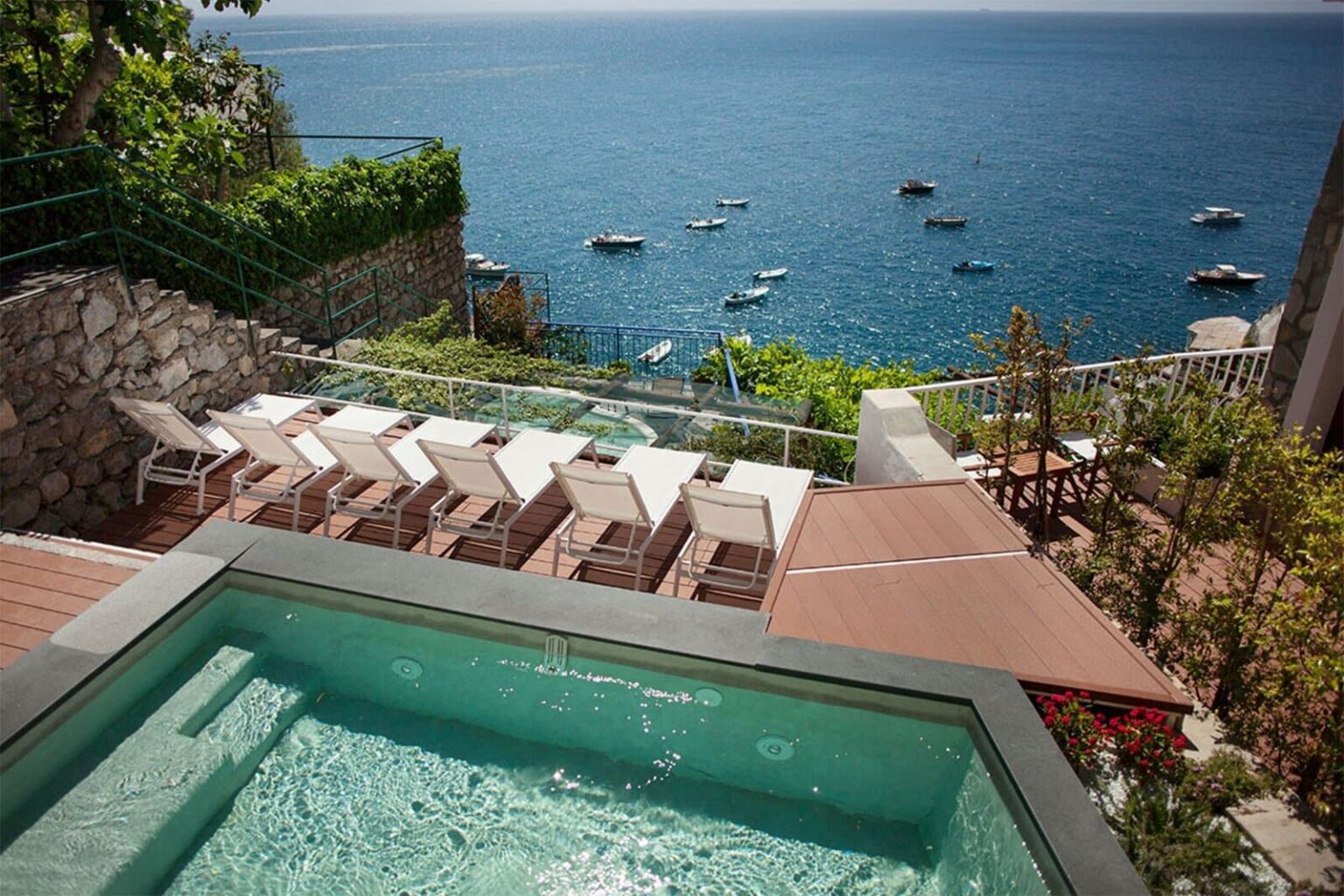 Luxury villa with a private pool overlooking the ocean, featuring sun loungers and boats in the water, surrounded by lush greenery. Ideal for a serene getaway or vacation rental. | Only on SopranoVillas